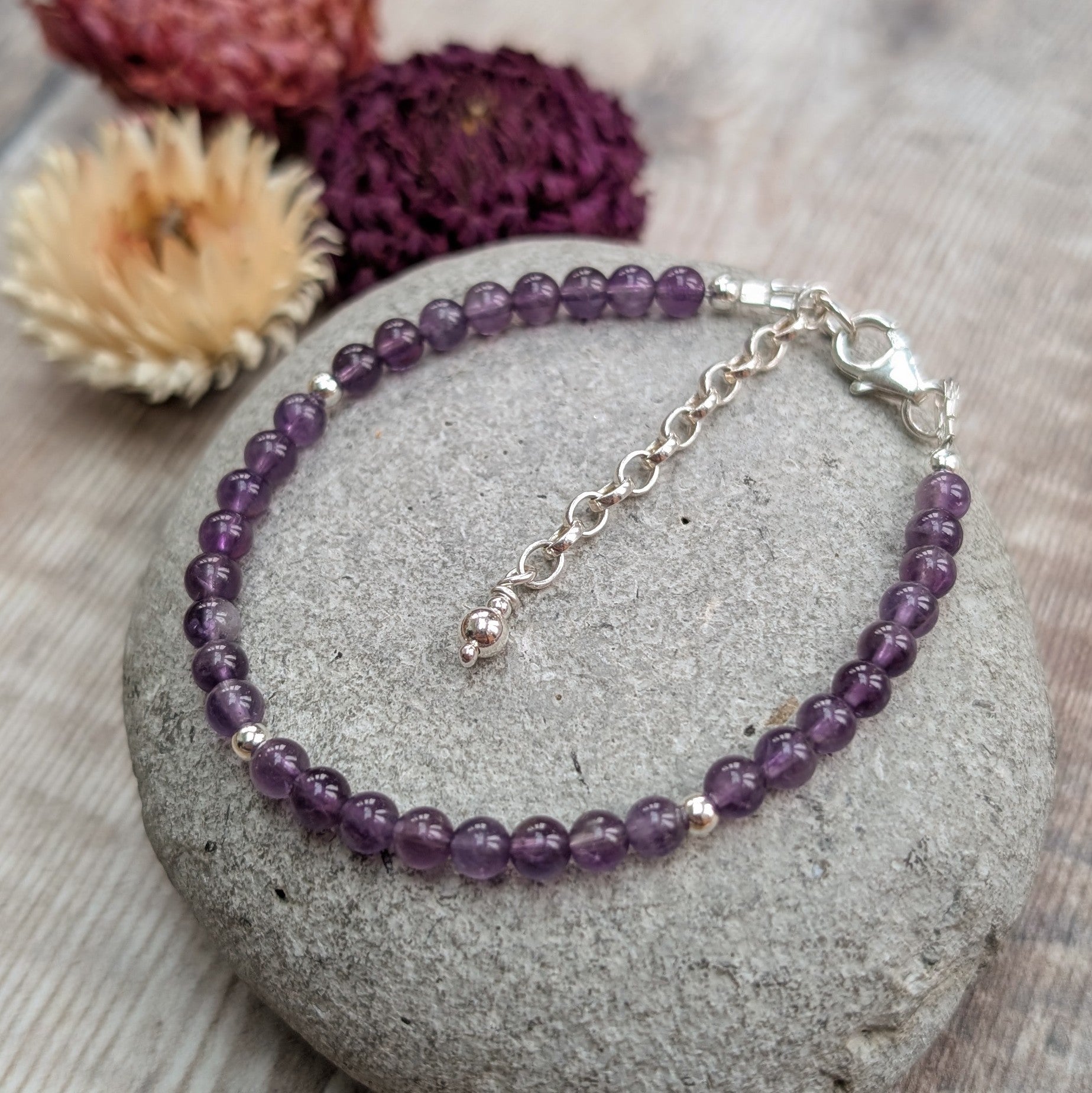Amethyst and sterling silver bead bracelet laid flat on a stone surface, with the silver extender chain and clasp clearly visible.