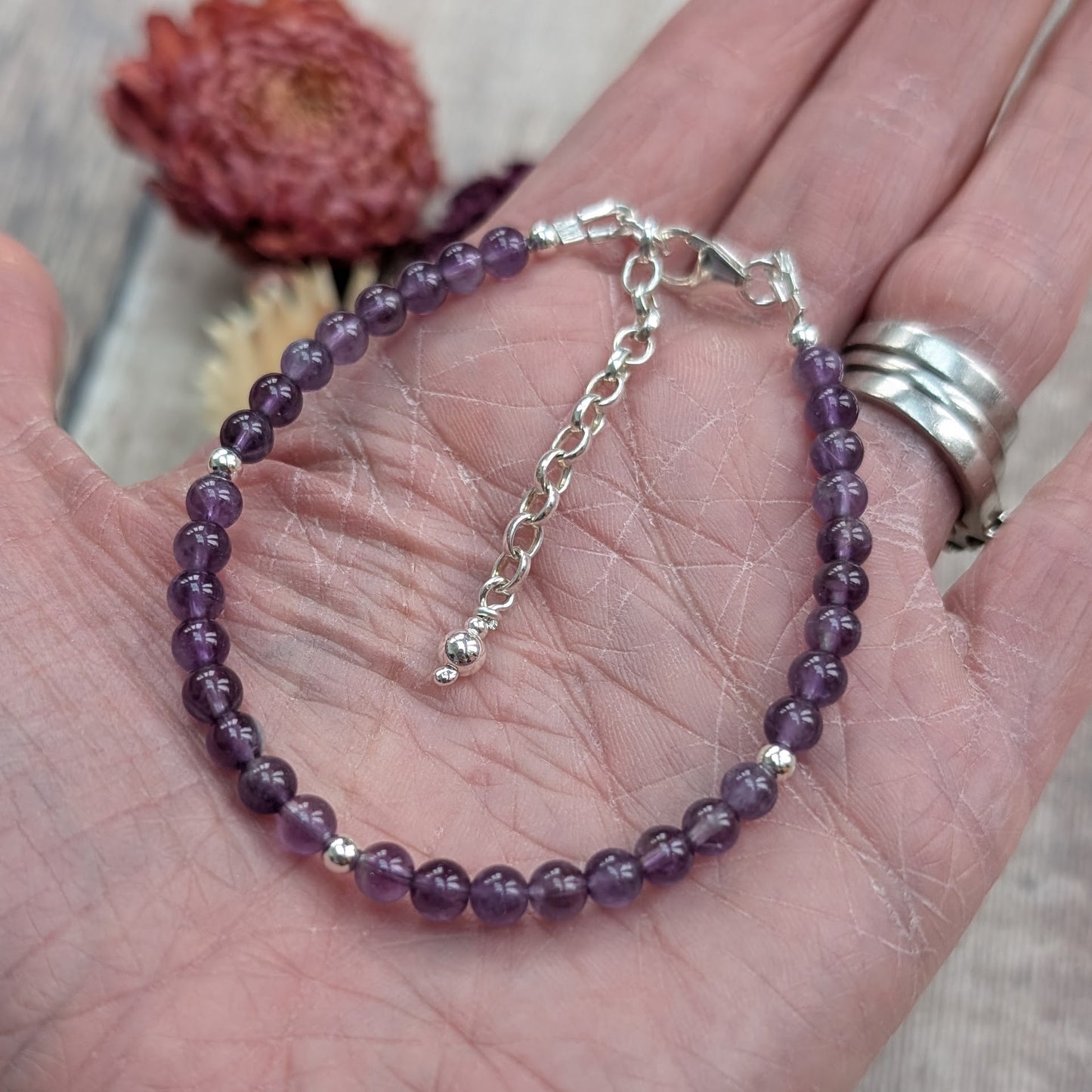 Sterling silver and amethyst bead bracelet shown resting in the palm of a hand, highlighting the lobster clasp and adjustable extender chain.