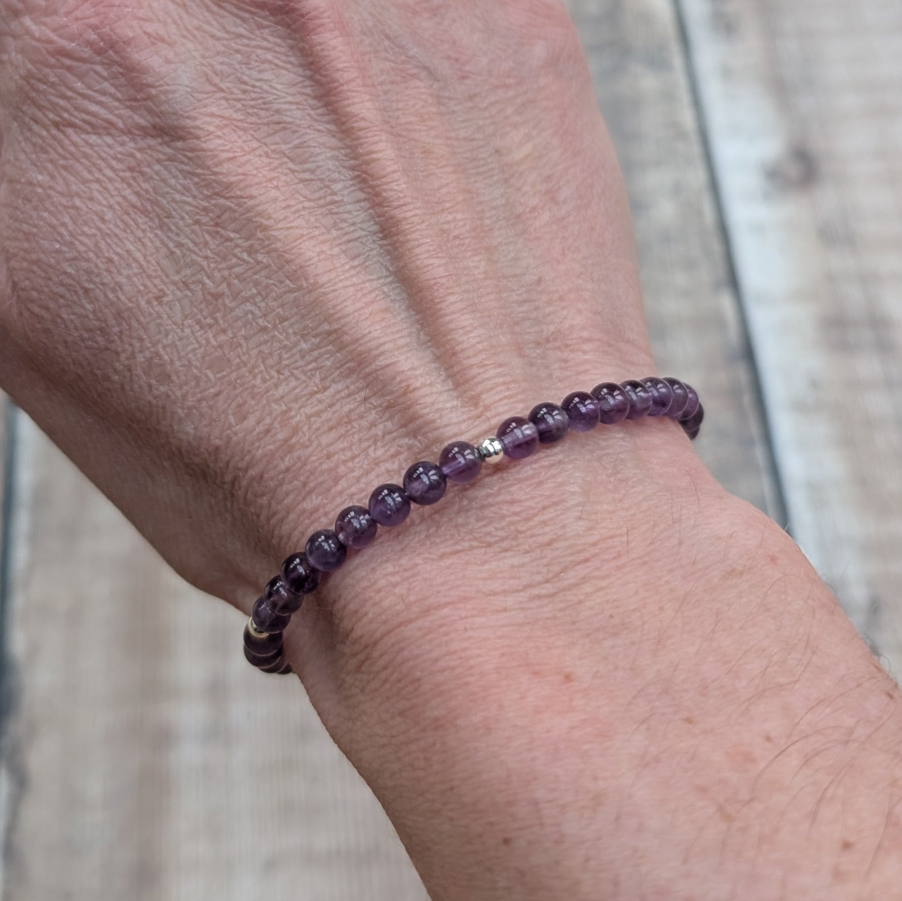 Close-up of an amethyst bead bracelet worn on the wrist, showing the smooth polished beads and single sterling silver spacer bead.