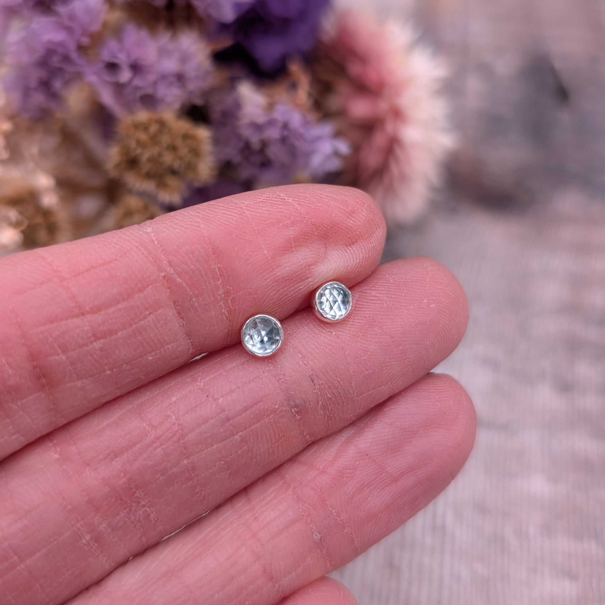 Each earring is a round rose cut Aquamarine gemstone set in silver bezel attached to stud bar. Stone is pale blue translucent with uneven rose cut finish that catches the light at different angles.