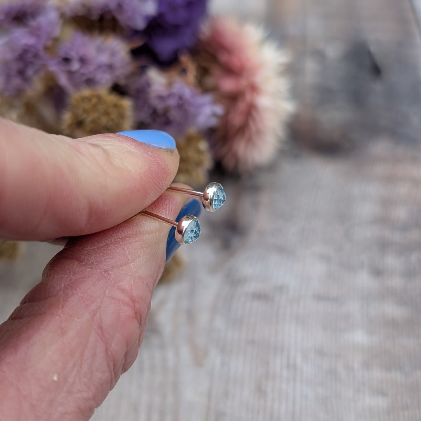 Each earring is a round rose cut Aquamarine gemstone set in silver bezel attached to stud bar. Stone is pale blue translucent with uneven rose cut finish that catches the light at different angles.