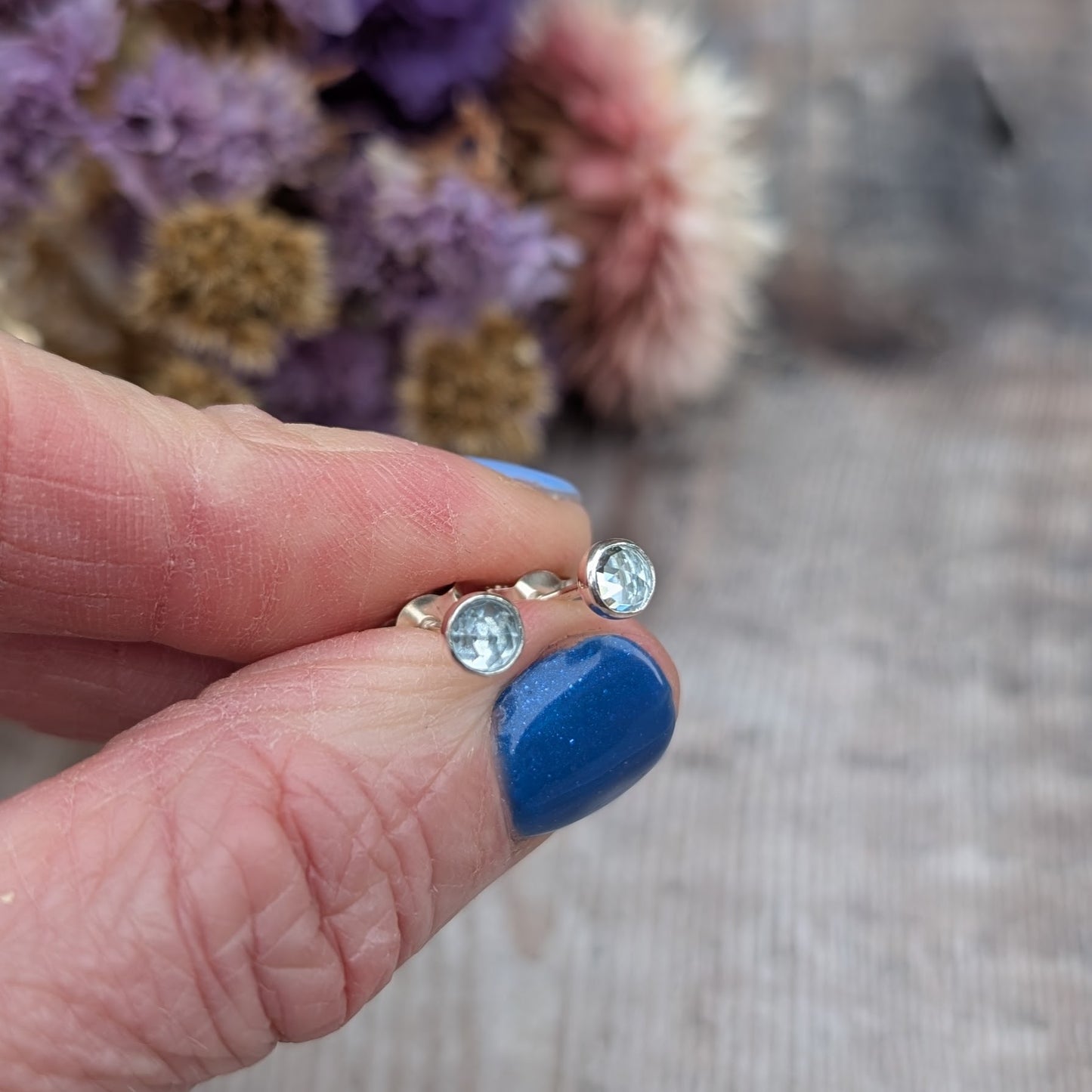 Each earring is a round rose cut Aquamarine gemstone set in silver bezel attached to stud bar. Stone is pale blue translucent with uneven rose cut finish that catches the light at different angles.