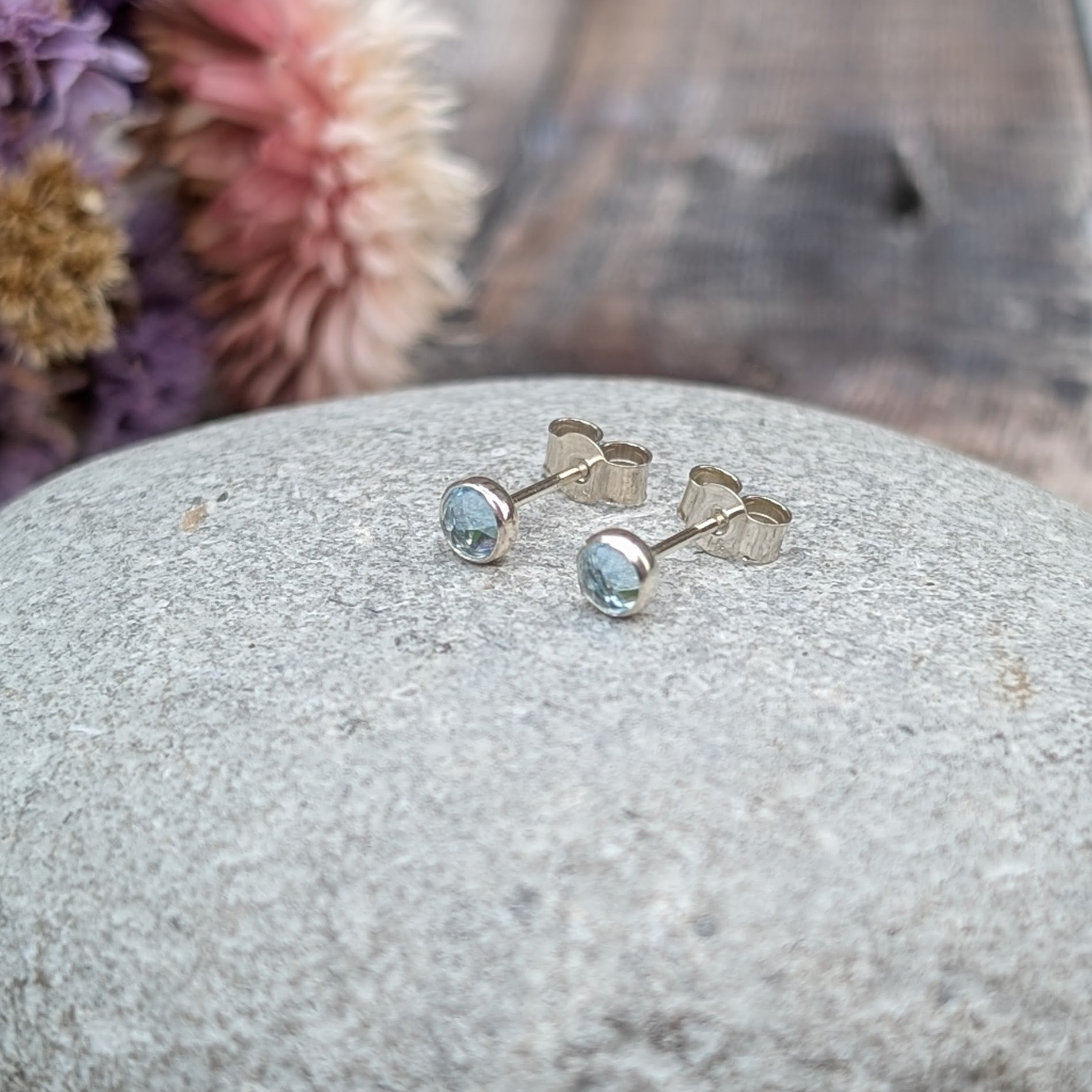 Each earring is a round rose cut Aquamarine gemstone set in silver bezel attached to stud bar. Stone is pale blue translucent with uneven rose cut finish that catches the light at different angles.