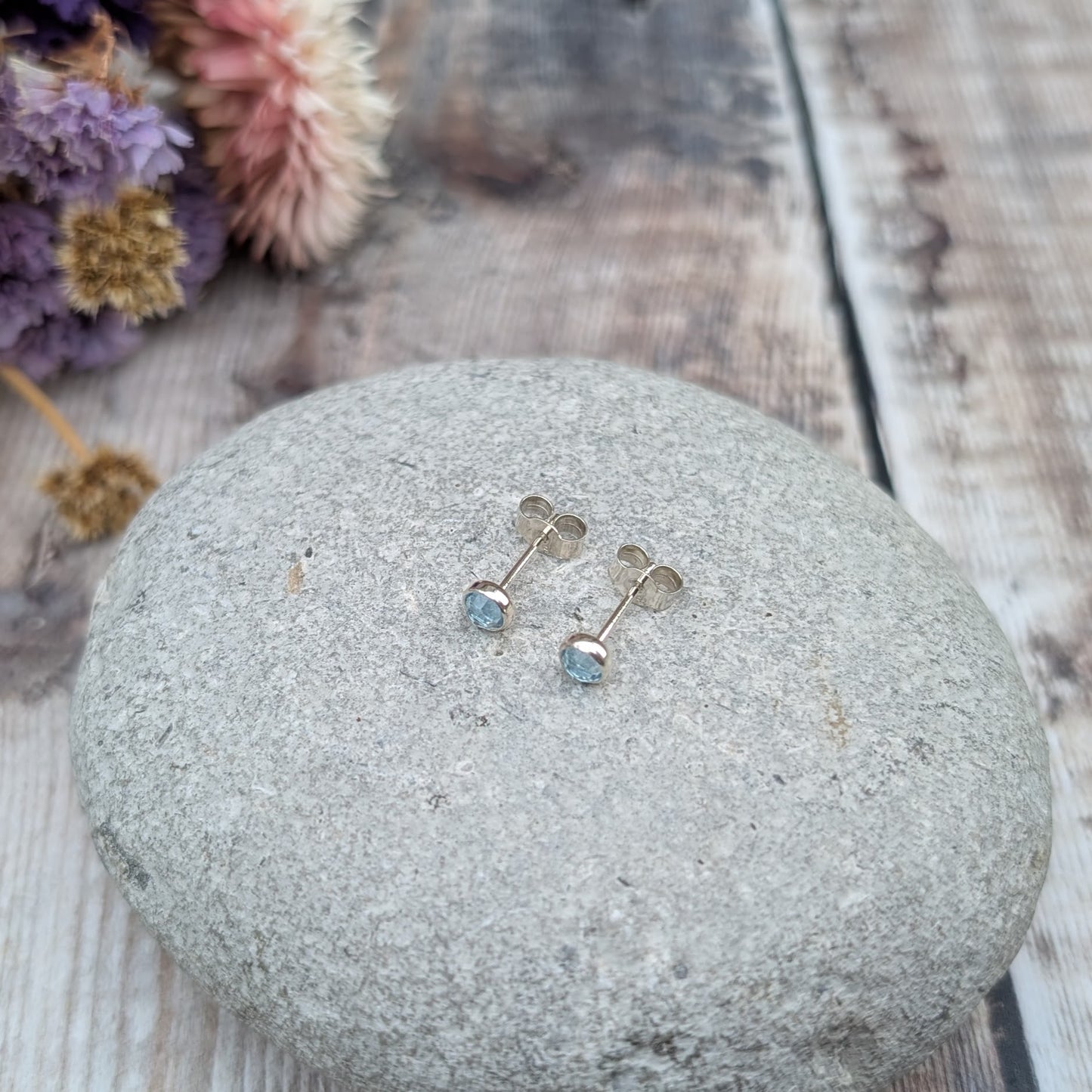 Each earring is a round rose cut Aquamarine gemstone set in silver bezel attached to stud bar. Stone is pale blue translucent with uneven rose cut finish that catches the light at different angles.