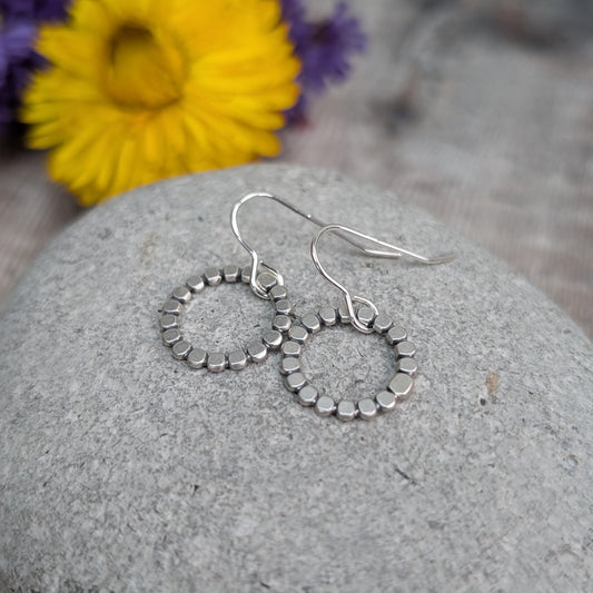 Each earring is a joined circle of small oxidised silver beads with flattened texture, suspended from silver earring wire.