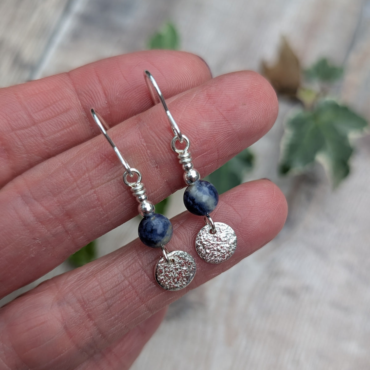 Close up of blue sodalite and silver textured disc earrings resting on fingers, showing the natural blue and white patterns of the sodalite beads, textured sterling silver discs and silver bead details.