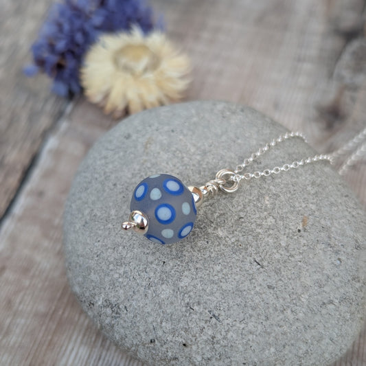Close-up of the Blue Spotty Lampwork Glass Necklace on a stone surface showing the handmade glass bead and recycled sterling silver fittings.