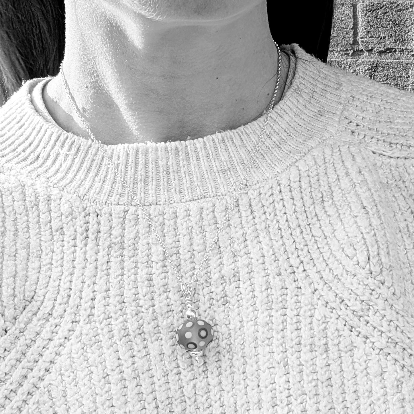 Blue Spotty Lampwork Glass Necklace worn on a chain around the neck with a knitted jumper.