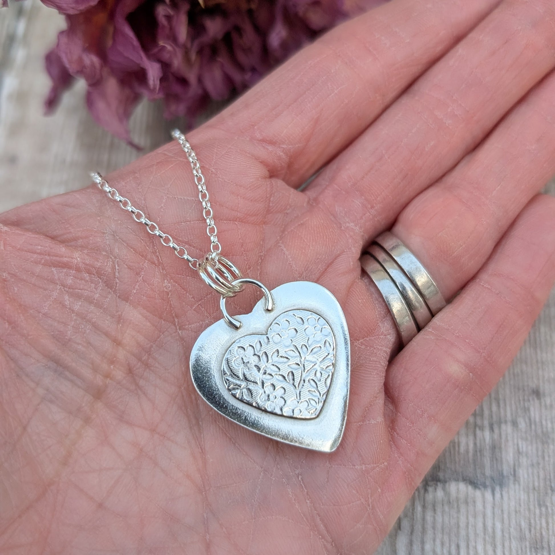 Pendant is blue heart shaped surfite set in a silver bezel surround, suspended from chain via two small open circle rings. Reverse of pendant has slightly raised heart shape stamped with floral pattern. Surfite is pale blue turquoise with white and darker blue flecks.