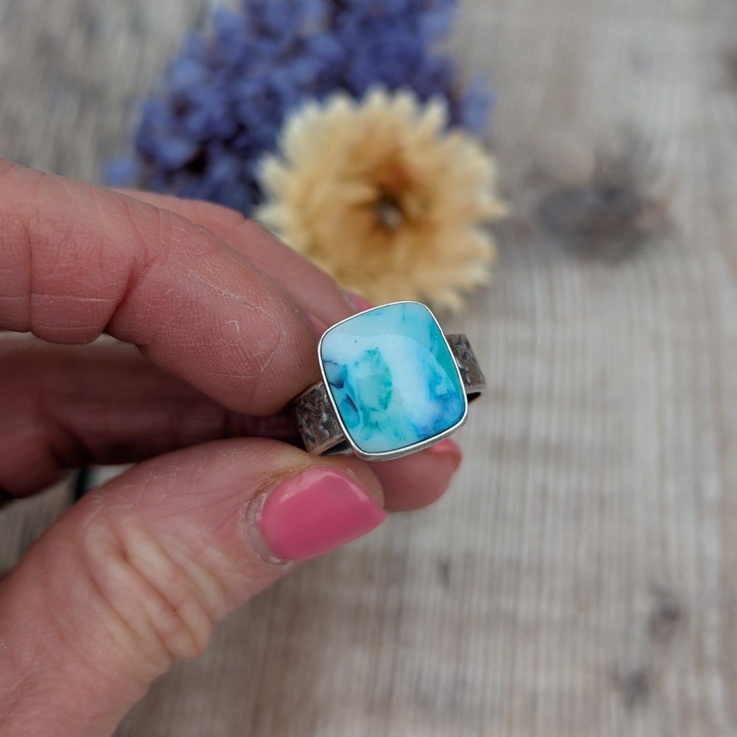 Blue Surfite Rectangle Ring with Silver Star Stamped Band held between fingers showing the front of the blue Surfite stone.