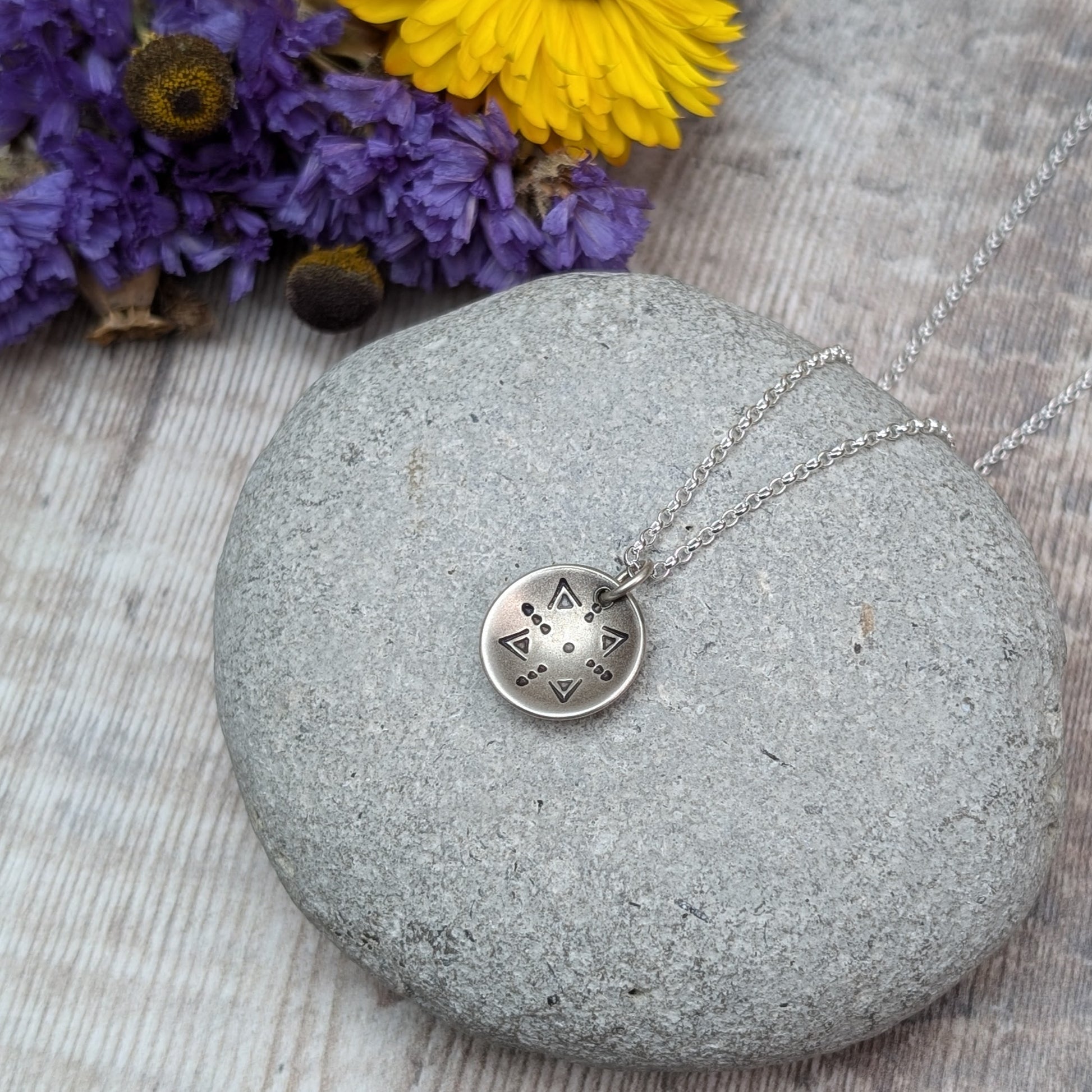 Oxidised Sterling Silver dome shaped pendant suspended from silver chain. Pendant has geometric triangular and dot patterns on the inside of the curved dome.