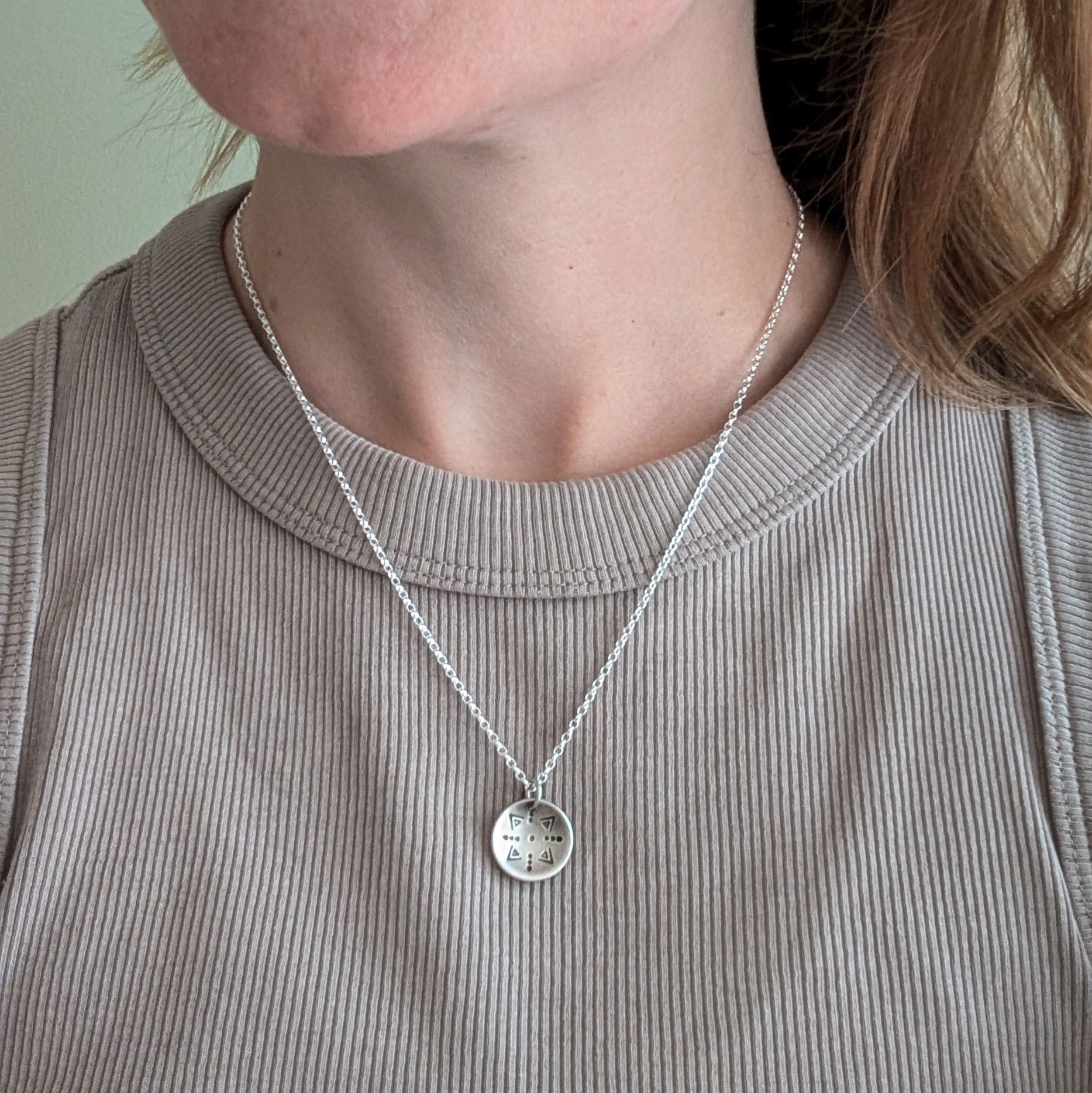 Oxidised Sterling Silver dome shaped pendant suspended from silver chain. Pendant has geometric triangular and dot patterns on the inside of the curved dome.