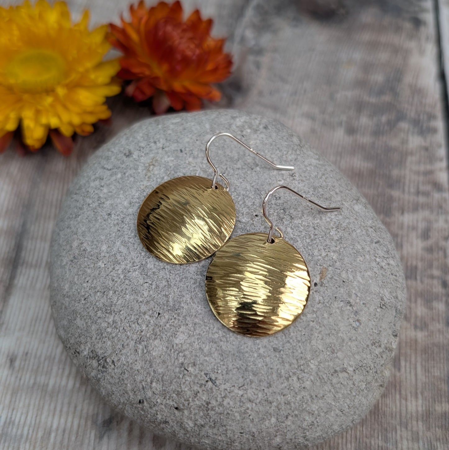 Hammered brass domed earrings displayed on a grey pebble, showing the reflective surface and sterling silver hooks.