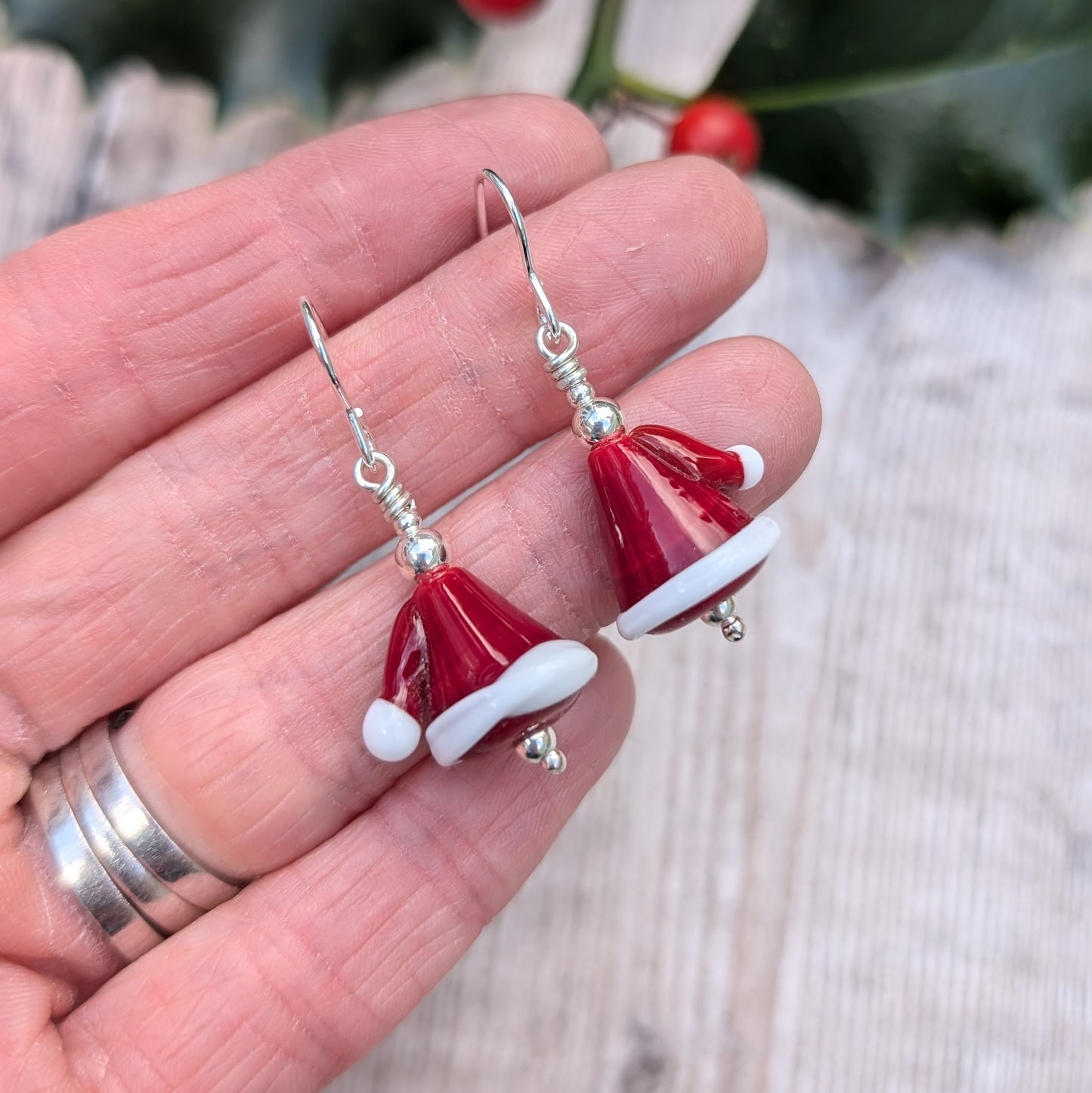 Each earring is a Santa hat-shape made from red and white lampwork glass. They are red with white trim and a small white pom-pom detail. Suspended from silver earring wire.