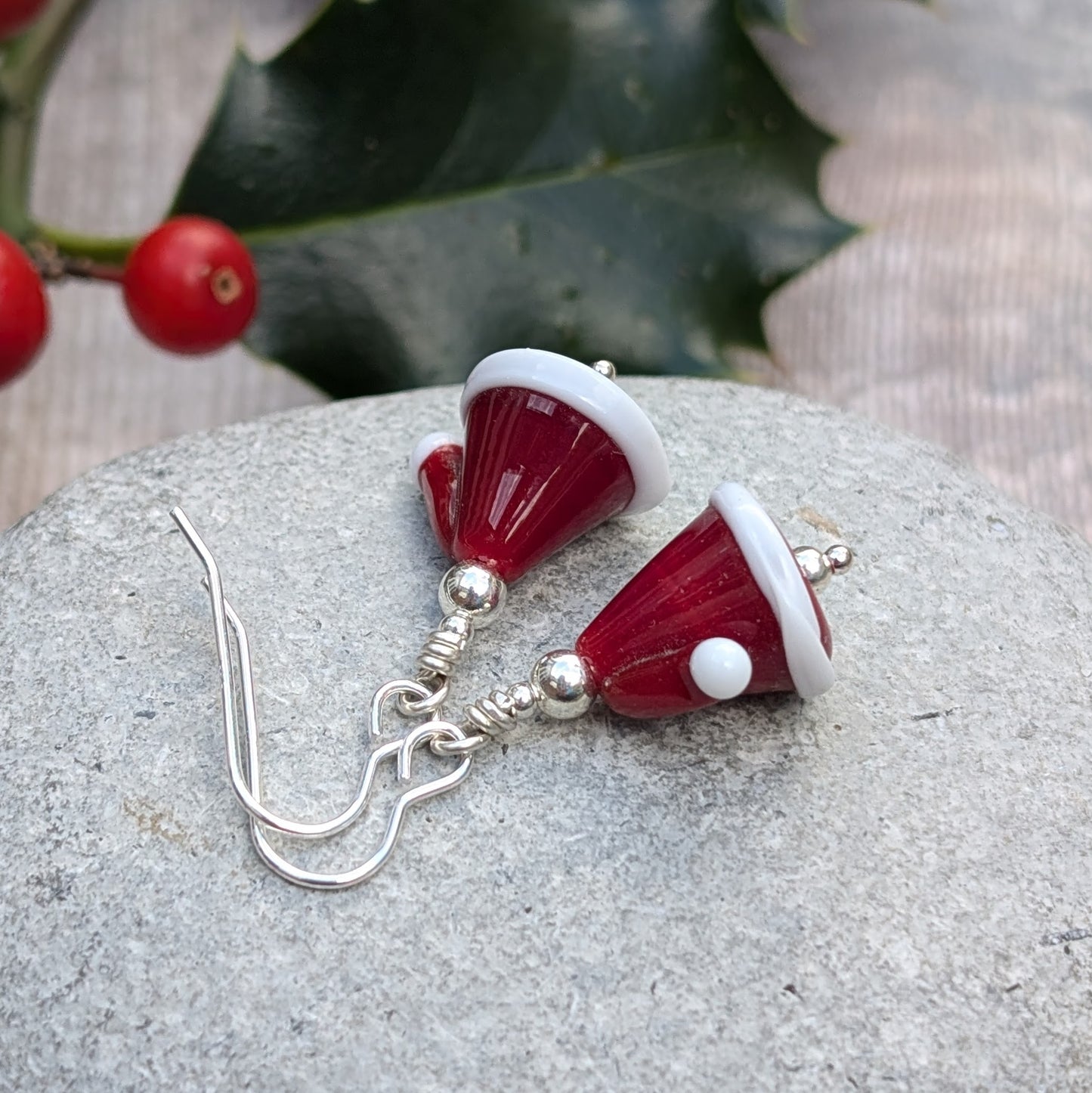 Each earring is a Santa hat-shape made from red and white lampwork glass. They are red with white trim and a small white pom-pom detail. Suspended from silver earring wire.