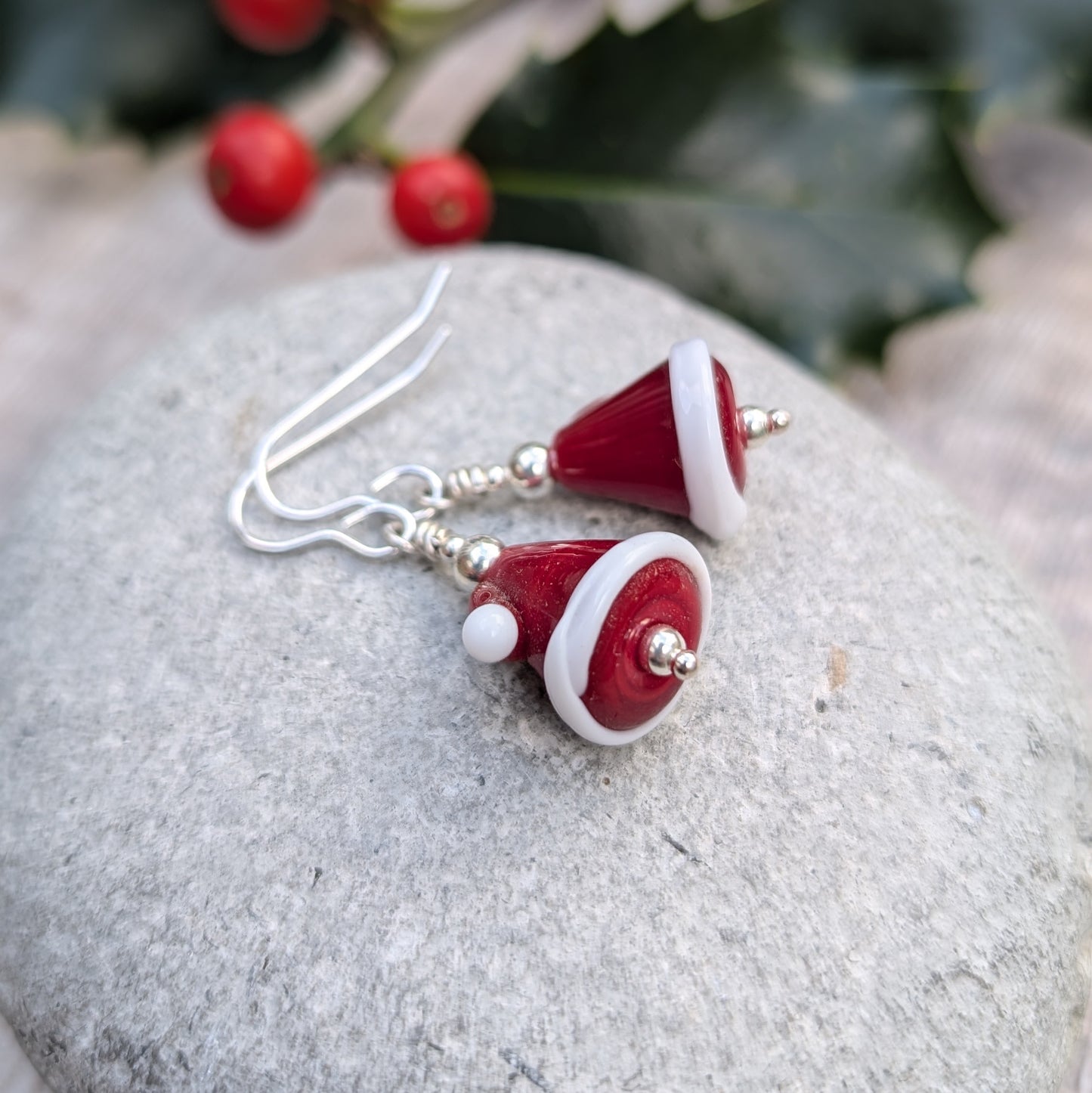 Each earring is a Santa hat-shape made from red and white lampwork glass. They are red with white trim and a small white pom-pom detail. Suspended from silver earring wire.