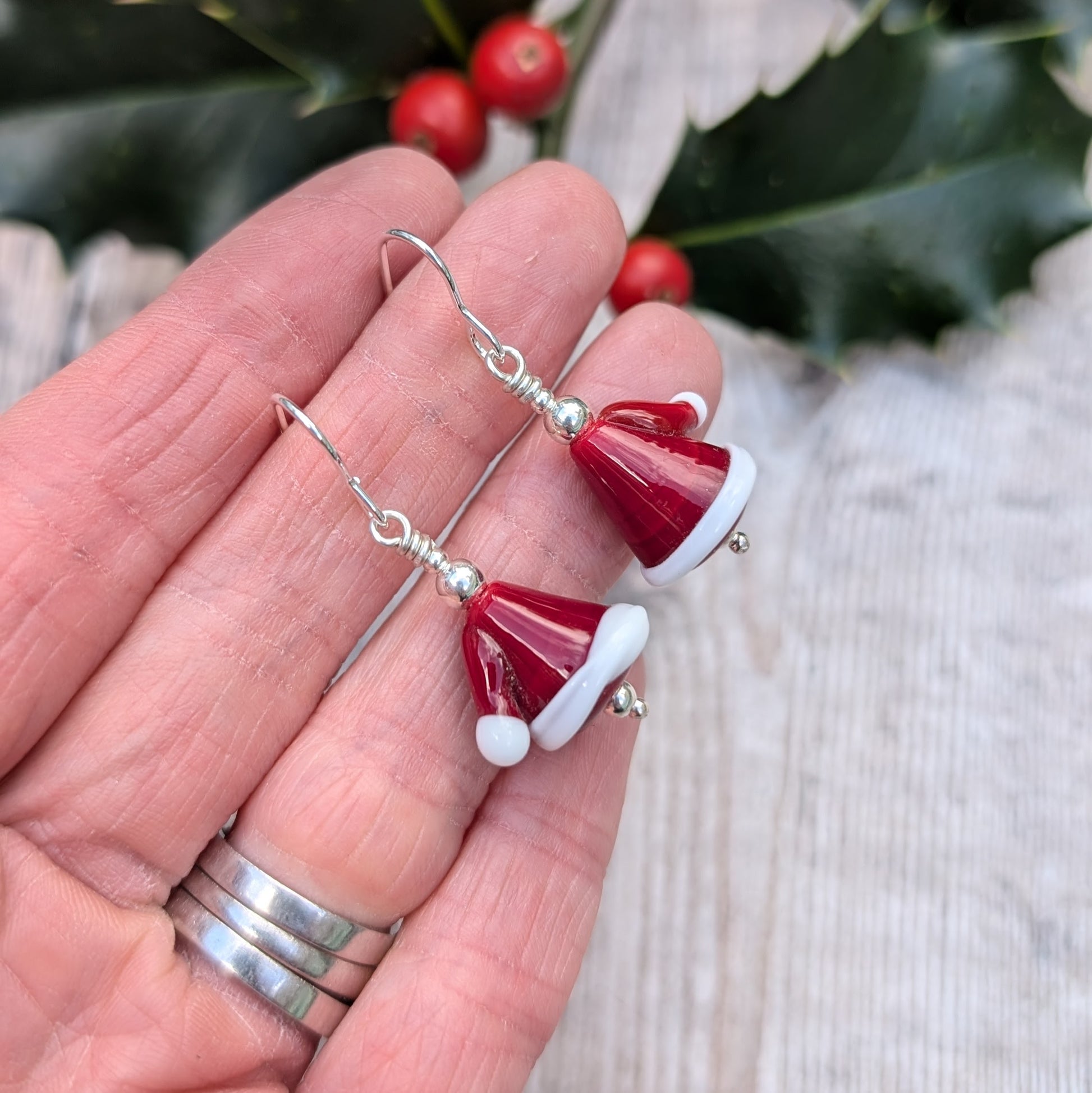 Each earring is a Santa hat-shape made from red and white lampwork glass. They are red with white trim and a small white pom-pom detail. Suspended from silver earring wire.