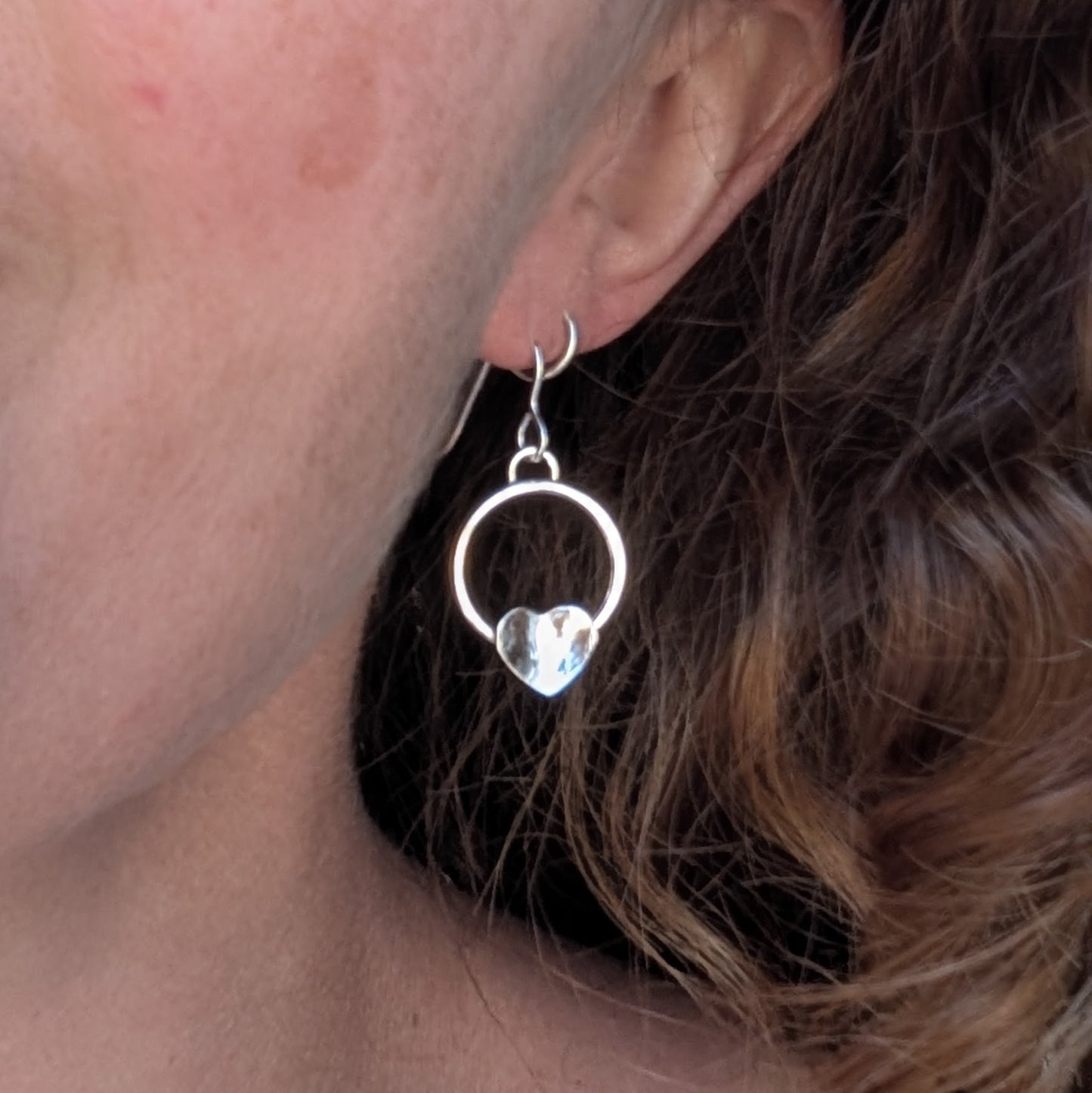 Circle earring with hammered hearts handmade from recycled Sterling Silver, worn on the ear to show the size and how they hang.