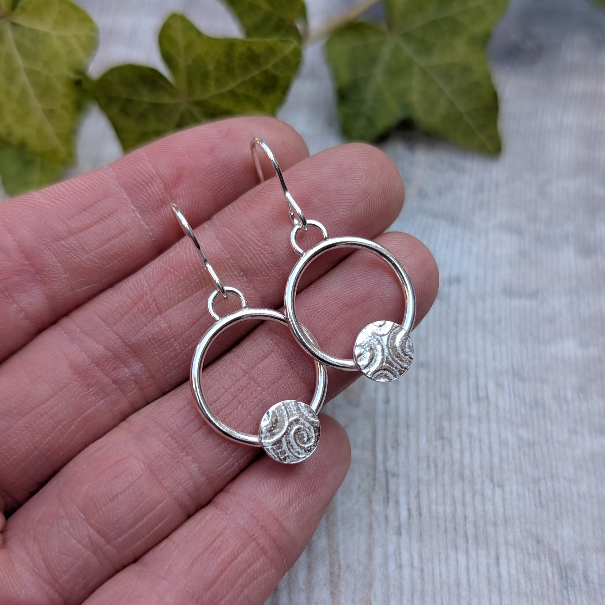 Circle earring with textured disc handmade from recycled Sterling Silver shown held in a hand to display size and detail.