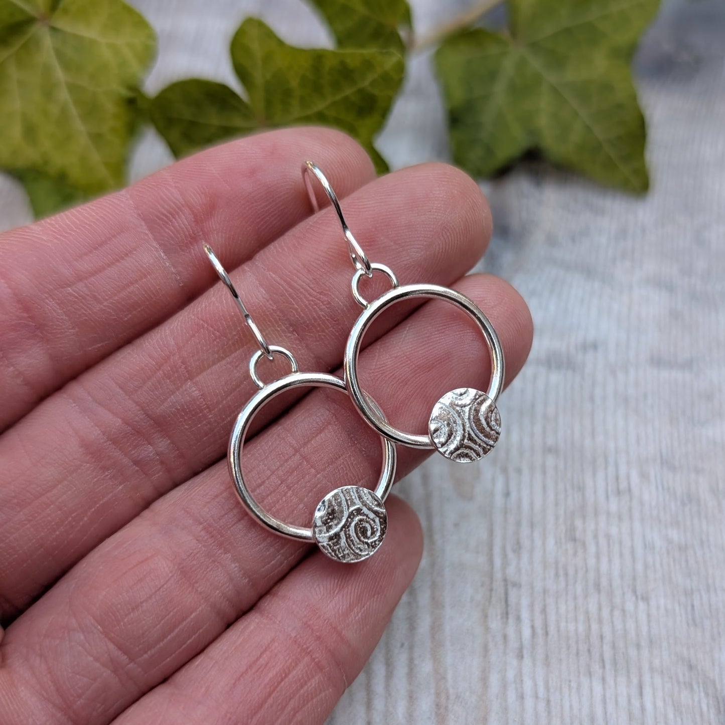 Close up of circle earring with textured disc handmade from recycled Sterling Silver held in a hand.