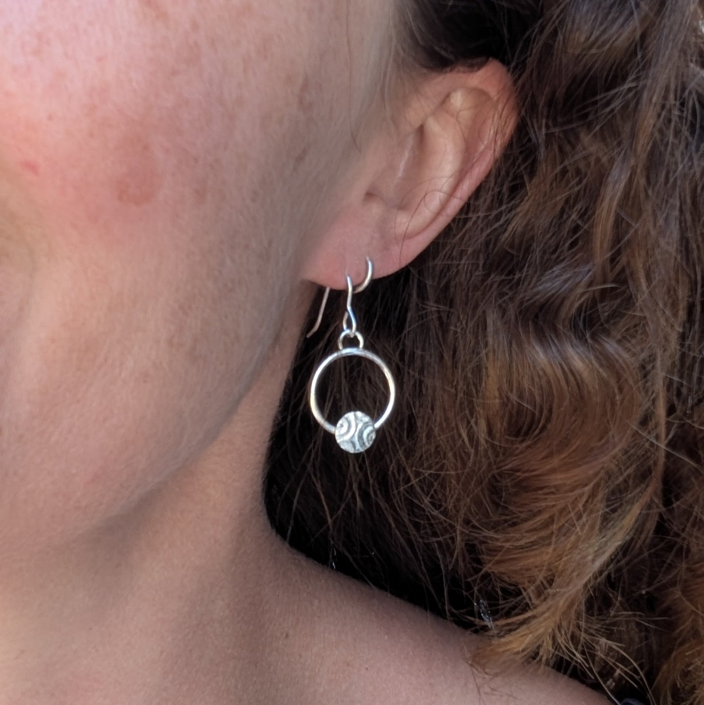 Circle earring with textured disc handmade from recycled Sterling Silver worn in the ear to show size and fit.