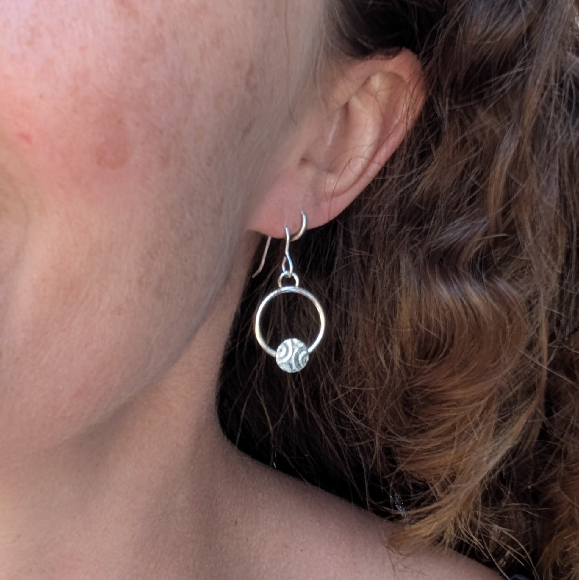 Circle earring with textured disc handmade from recycled Sterling Silver worn in the ear to show size and fit.