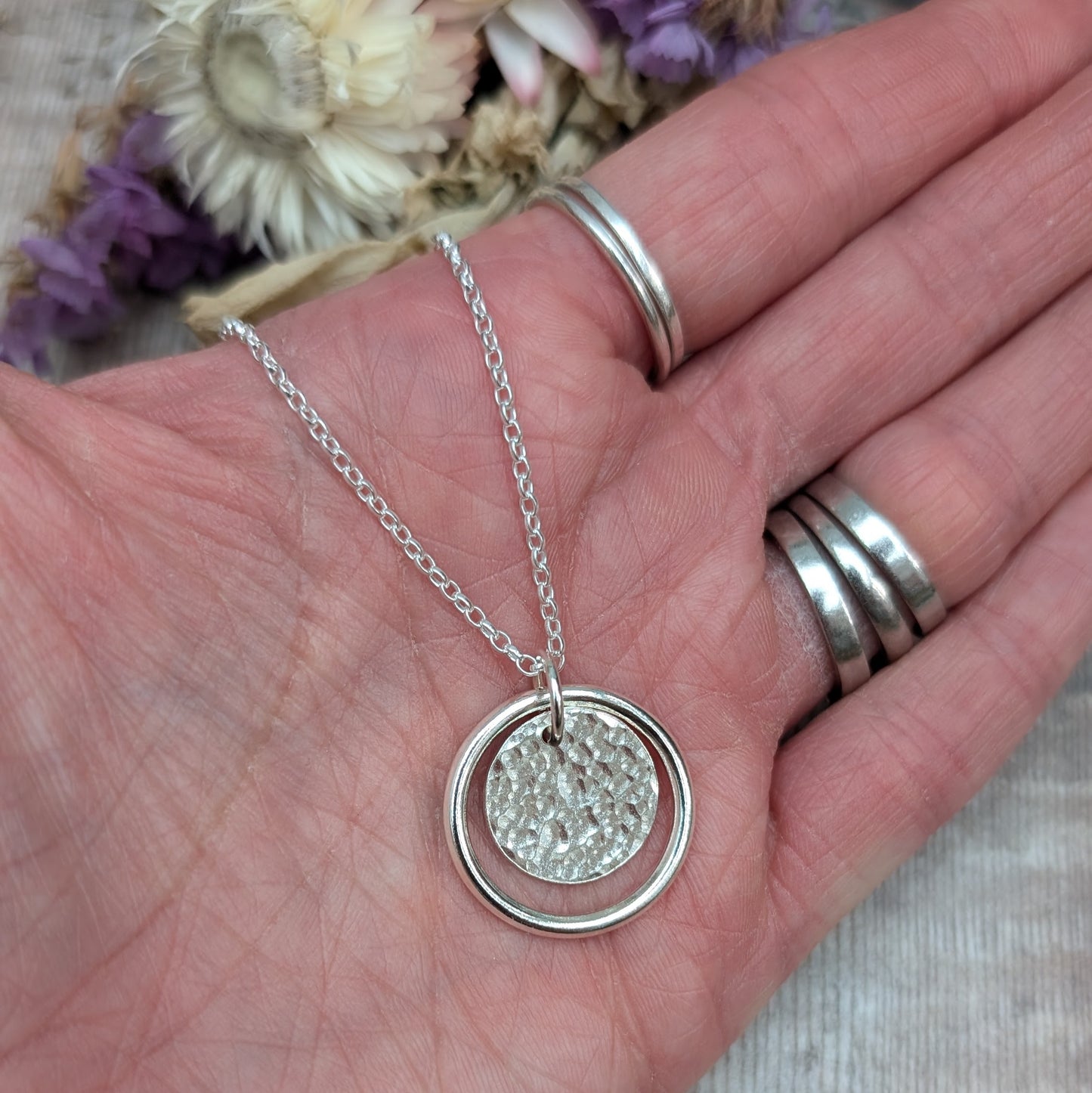 Sterling Silver smooth circle pendant with hammered silver disc sitting inside, suspended from a silver circle link attached to silver chain. 