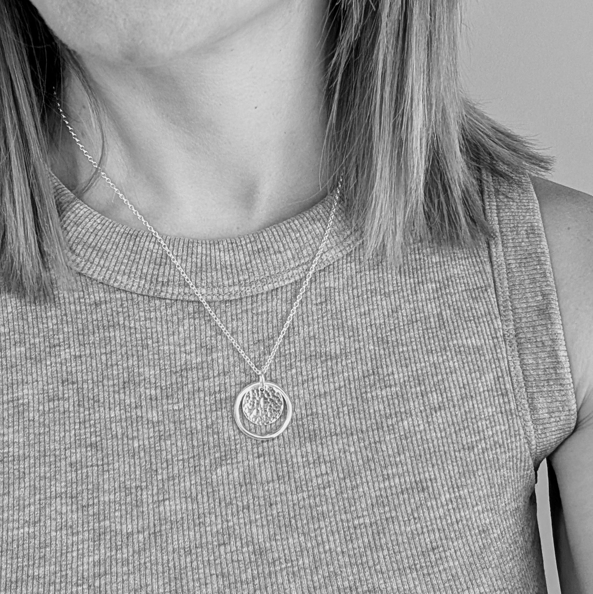 Sterling Silver smooth circle pendant with hammered silver disc sitting inside, suspended from a silver circle link attached to silver chain. 