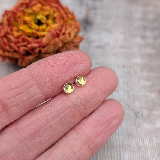 A pair of citrine stud earrings held in a hand, showing their compact design and shimmering gemstones.