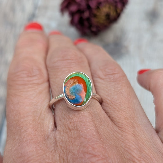A colourful oval Surfite ring in recycled sterling silver, shown worn on a hand with red painted nails.