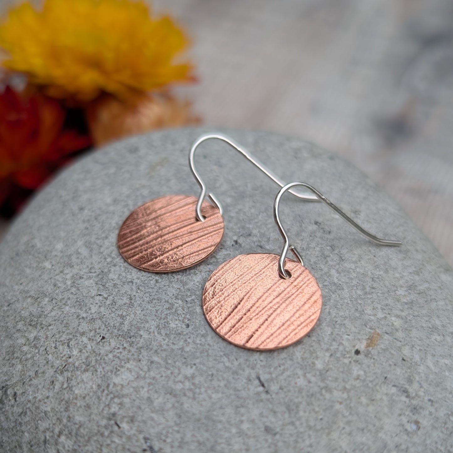 Close up of Copper bark pattern disc earrings on a grey stone highlighting the hand pressed bark pattern.
