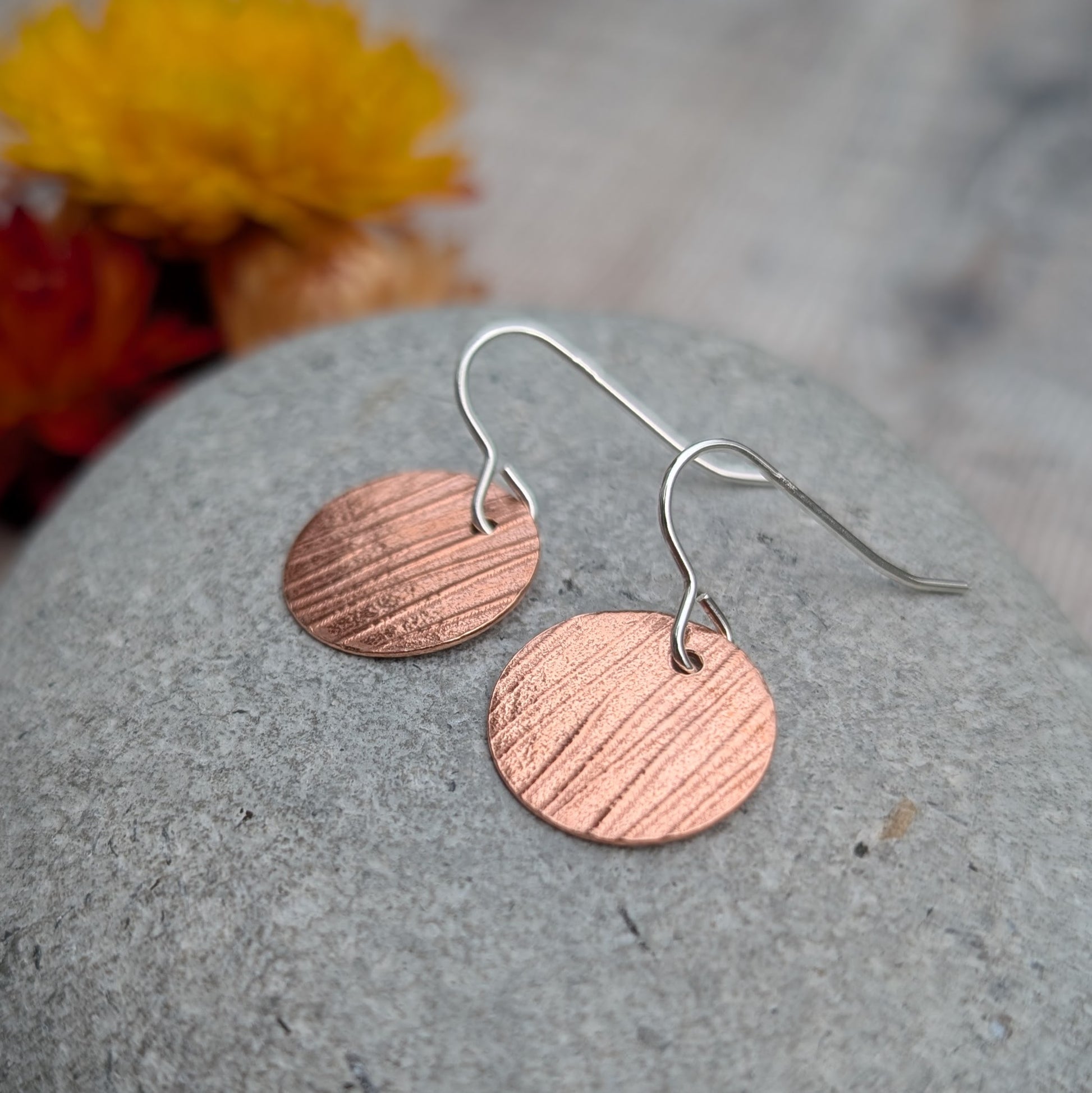 Close up of Copper bark pattern disc earrings on a grey stone highlighting the hand pressed bark pattern.