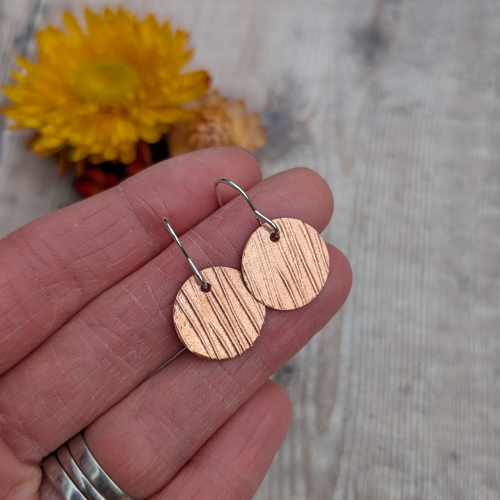 Copper bark pattern disc earrings held in a hand to show size and detail of the pressed bark texture.
