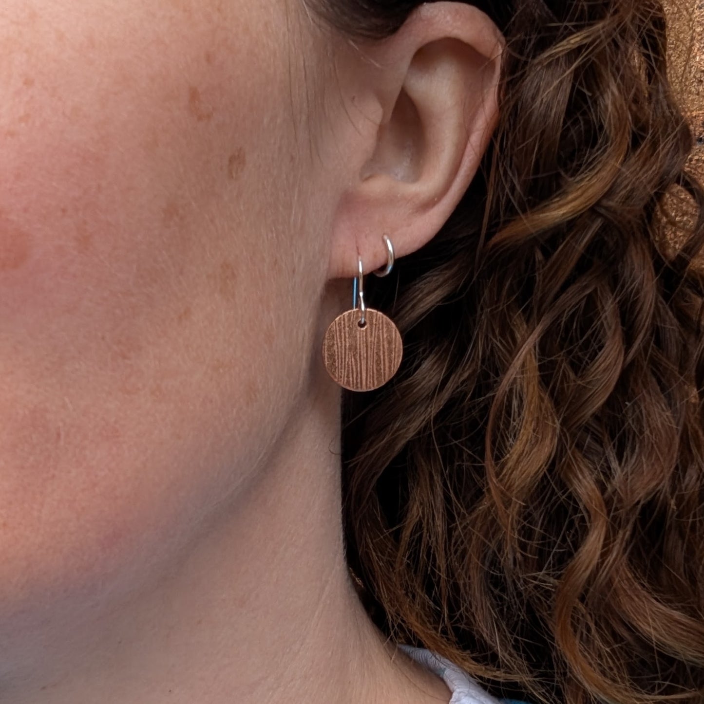 Copper bark pattern disc earrings worn on the ear showing how they hang when worn.