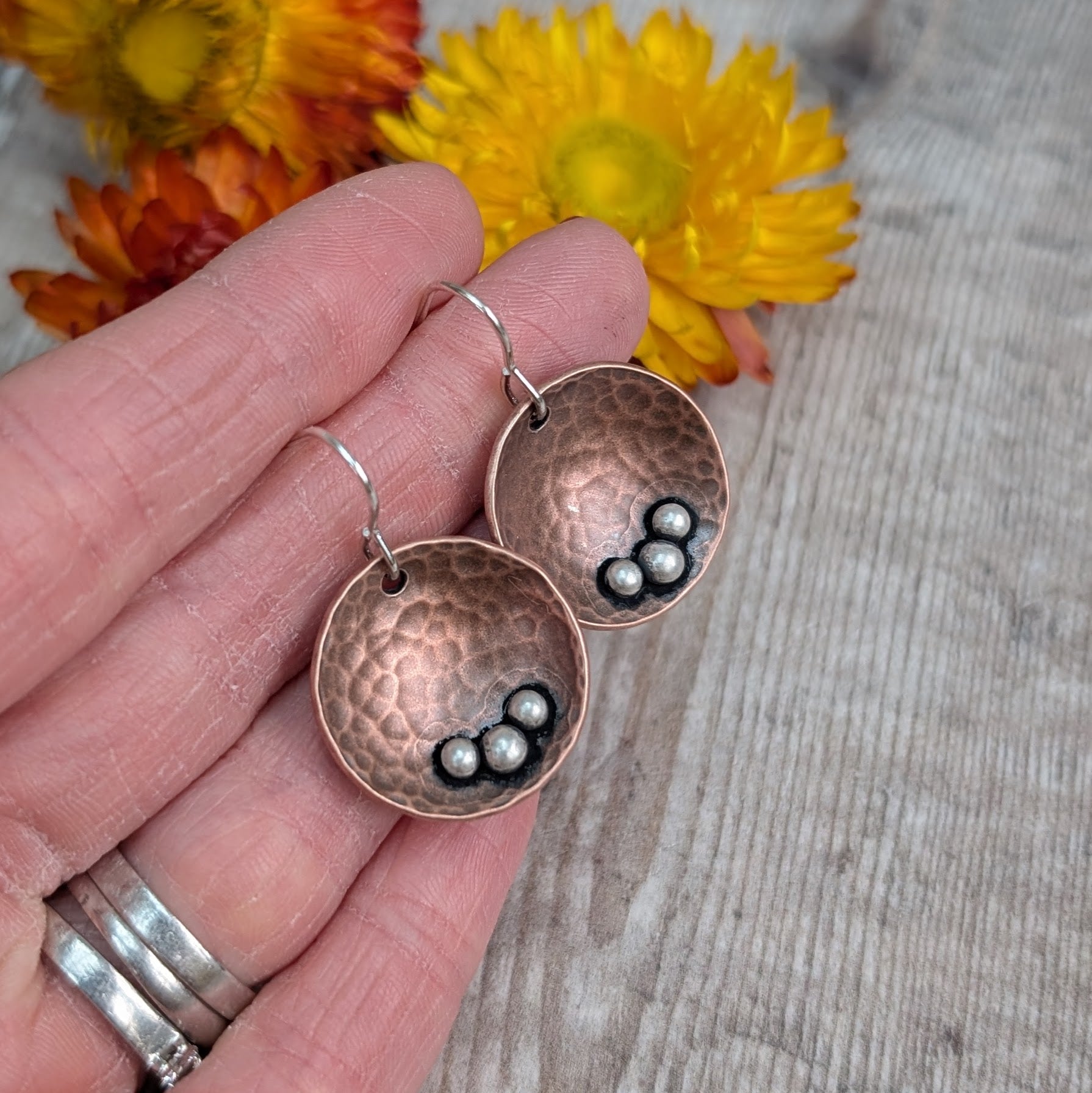 Each earring is an inverted copper hammered disc with three small silver pebbles on the lower curve of the disc. The hammered texture is accentuated by the oxidised copper. Suspended from silver earring wire.