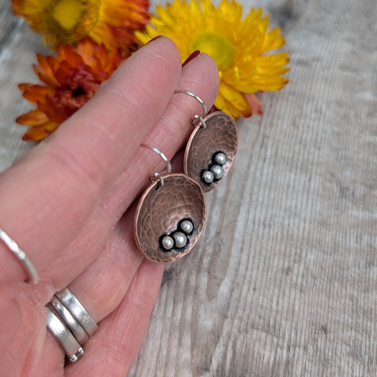 Each earring is an inverted copper hammered disc with three small silver pebbles on the lower curve of the disc. The hammered texture is accentuated by the oxidised copper. Suspended from silver earring wire.