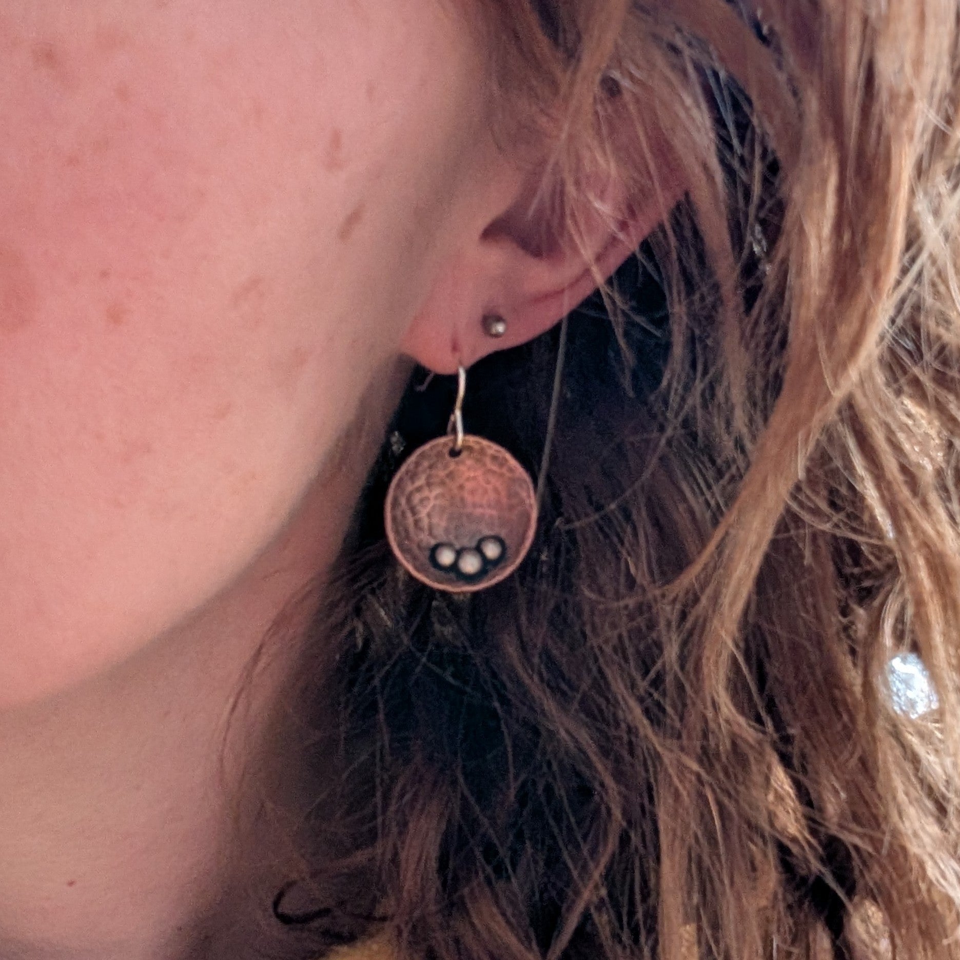 Each earring is an inverted copper hammered disc with three small silver pebbles on the lower curve of the disc. The hammered texture is accentuated by the oxidised copper. Suspended from silver earring wire.