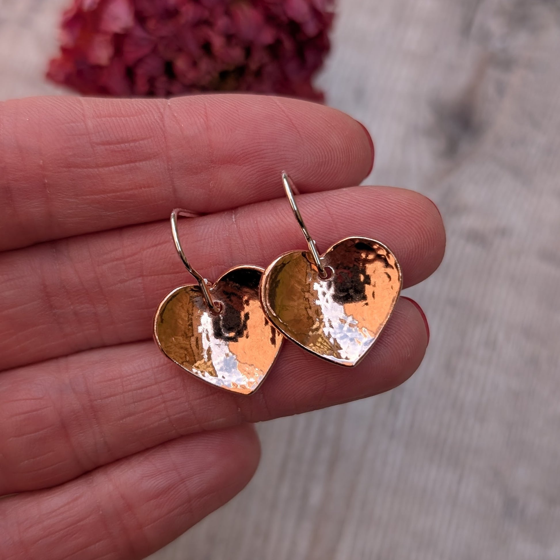 Two hammered copper heart earrings held together in a hand, highlighting their warm, polished finish.