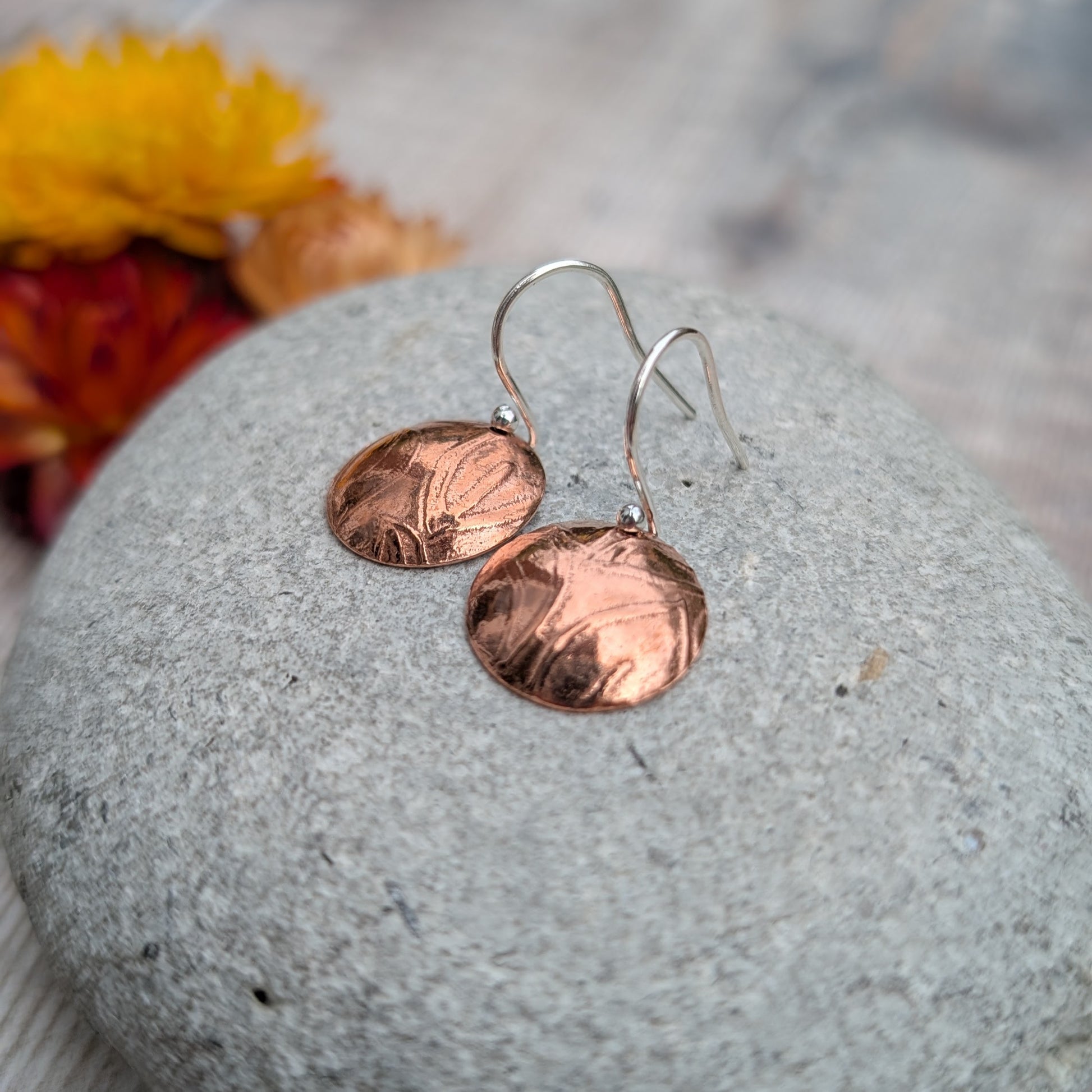Close up of Copper large leaf pattern dome disc earrings on a grey stone showing the domed form and pattern.