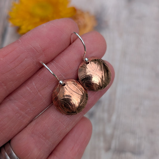 Copper large leaf pattern dome disc earrings held in a hand to show size and domed shape.