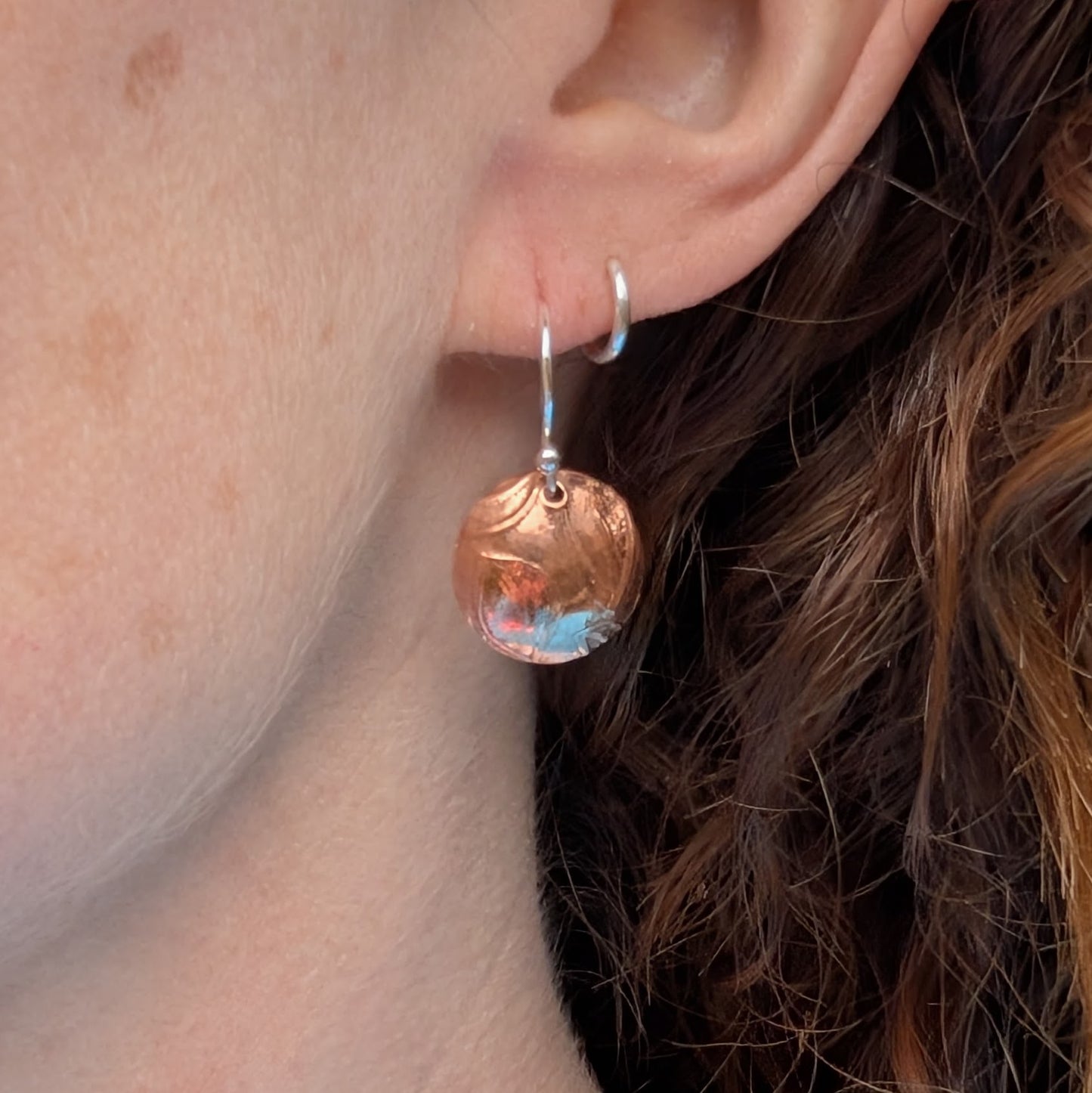 Copper large leaf pattern dome disc earrings worn on the ear showing how they hang when worn.