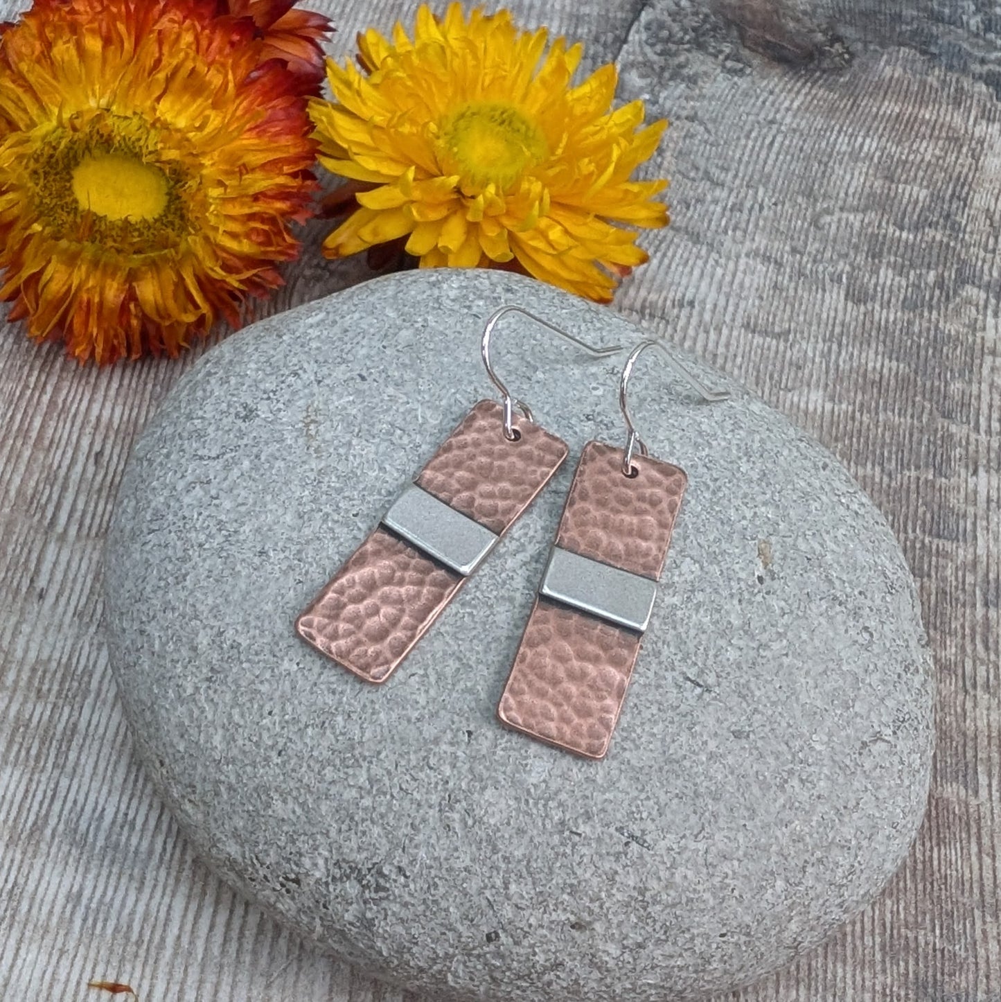 Each earring is a copper rectangle with a hammered oxidised finish. In the middle of the rectangle, there is a slightly raised silver strip. 