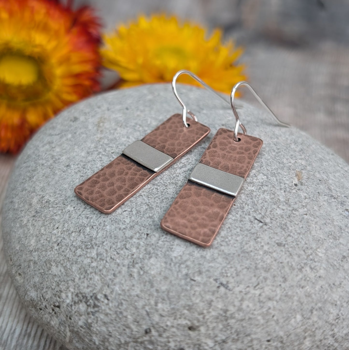 Each earring is a copper rectangle with a hammered oxidised finish. In the middle of the rectangle, there is a slightly raised silver strip. 