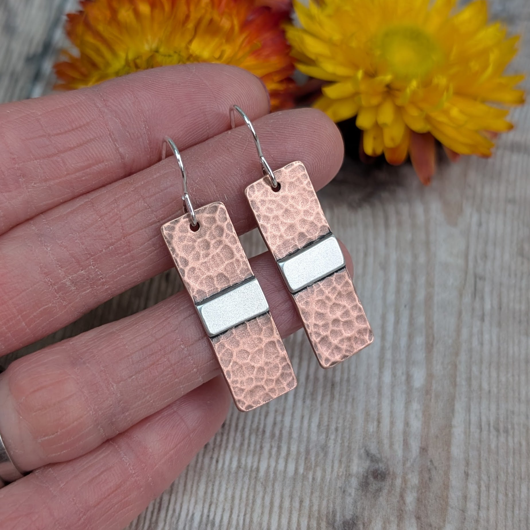 Each earring is a copper rectangle with a hammered oxidised finish. In the middle of the rectangle, there is a slightly raised silver strip. 