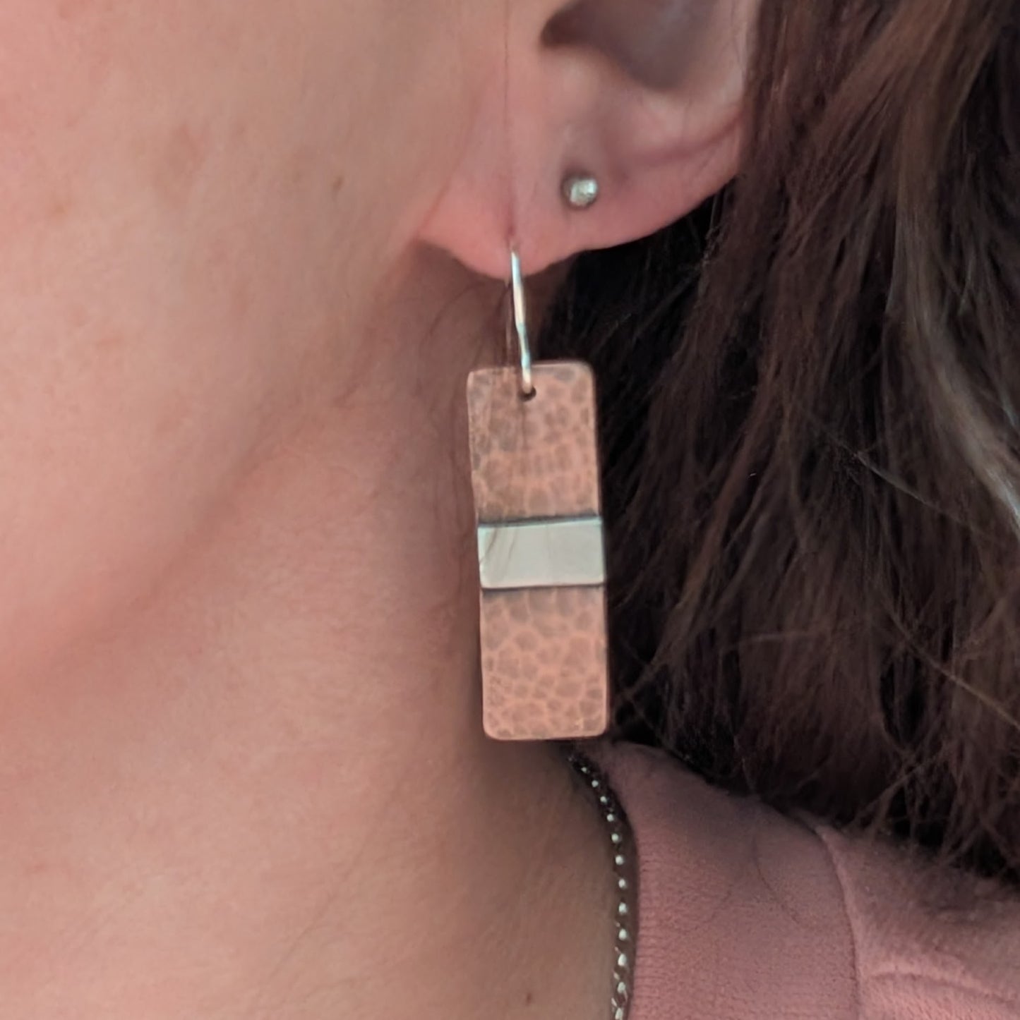 Each earring is a copper rectangle with a hammered oxidised finish. In the middle of the rectangle, there is a slightly raised silver strip. 