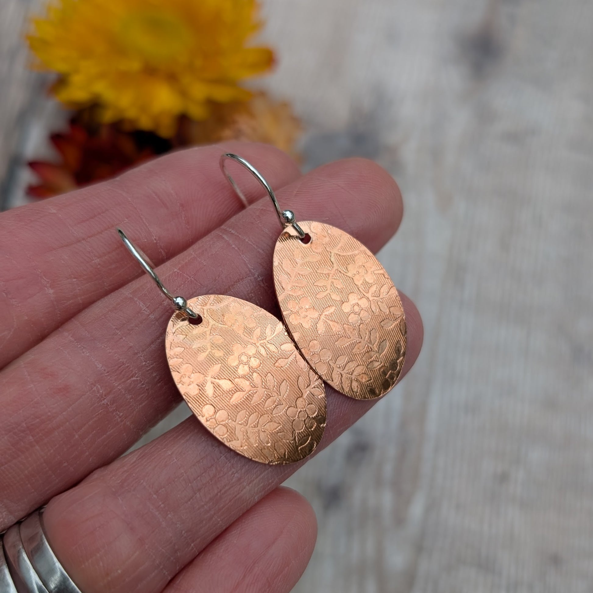 Close up of Copper floral pattern oval disc earrings in hand highlighting the pressed floral design.