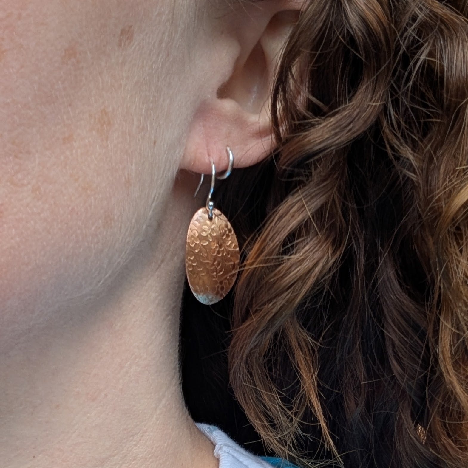 Copper floral pattern oval disc earrings worn on the ear showing how they hang.