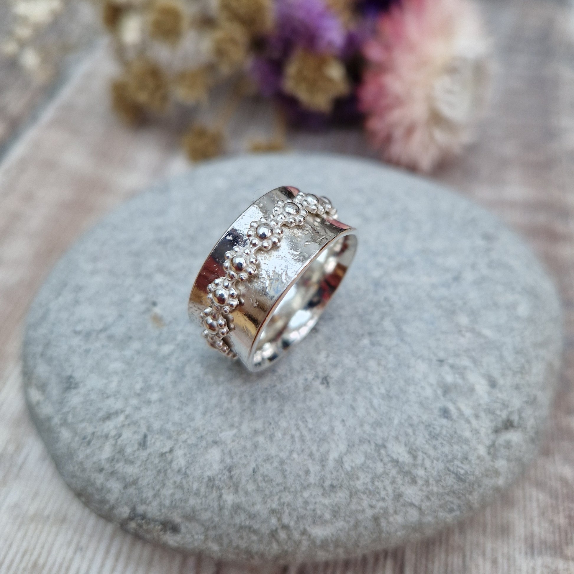  Approx. 10mm wide textured silver band with additional silver ring around the middle that spins independently detailed with repeating daisy flowers.