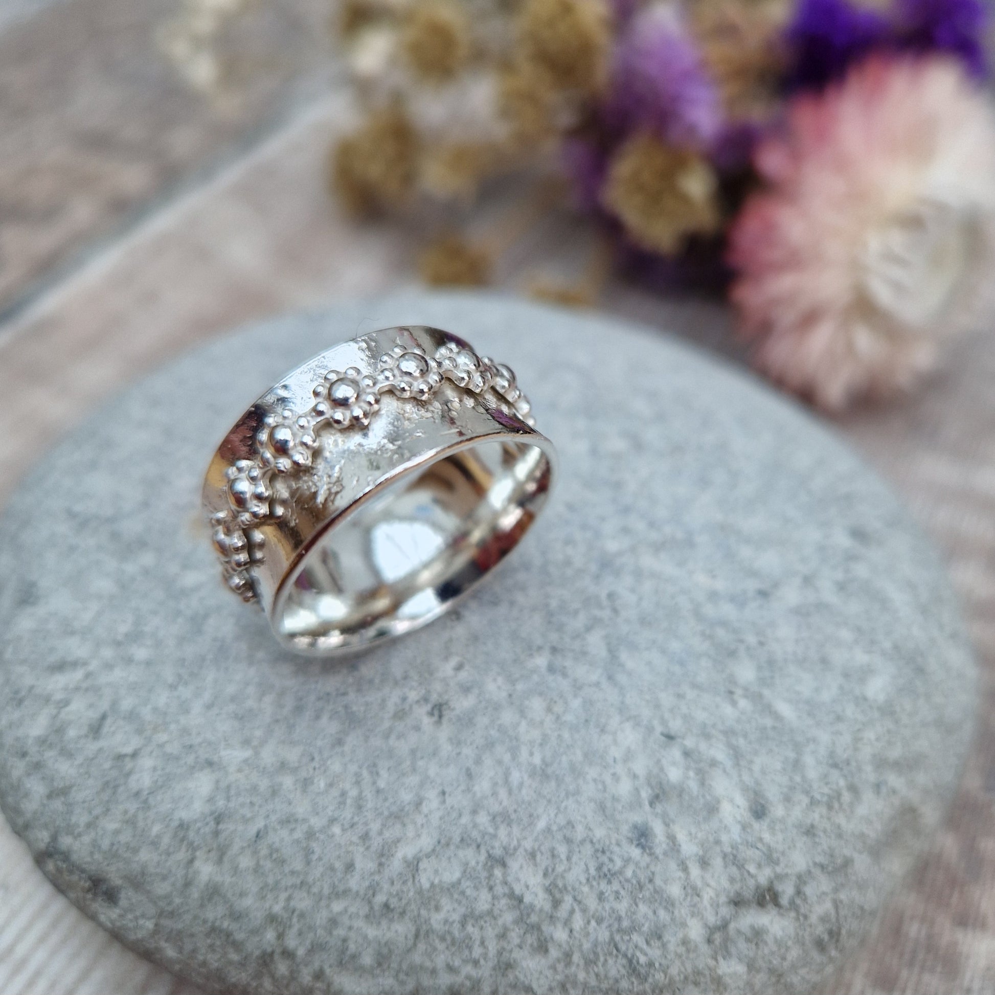  Approx. 10mm wide textured silver band with additional silver ring around the middle that spins independently detailed with repeating daisy flowers.