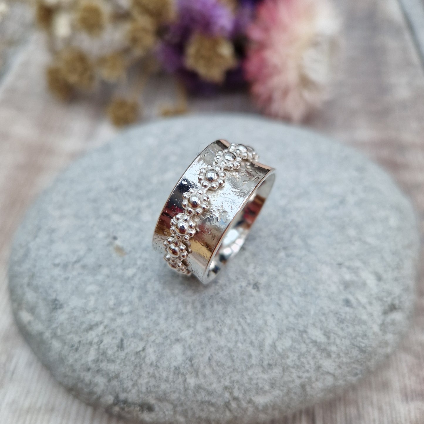  Approx. 10mm wide textured silver band with additional silver ring around the middle that spins independently detailed with repeating daisy flowers.